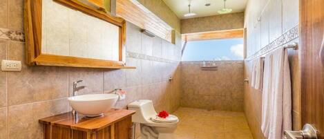 A bathroom with a wooden vanity, a white sink, a toilet, and a shower area.