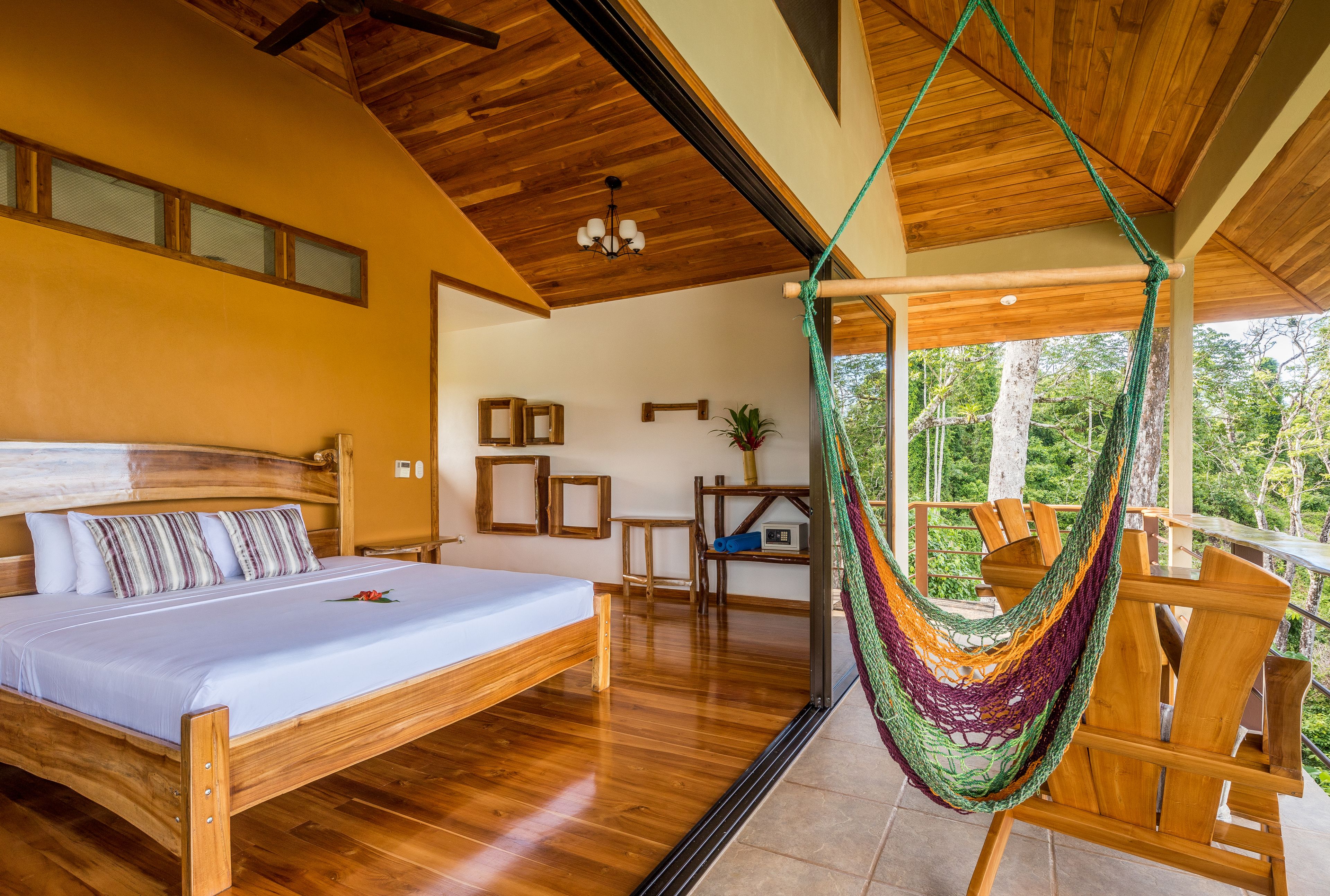 A bedroom with a wooden bed, a hammock, and a balcony with a view of trees.