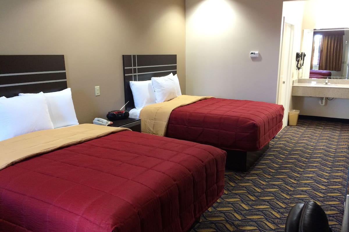 A hotel room with two beds, a bedside table with a radio, a mirror, and a bathroom with a sink and towel rack.