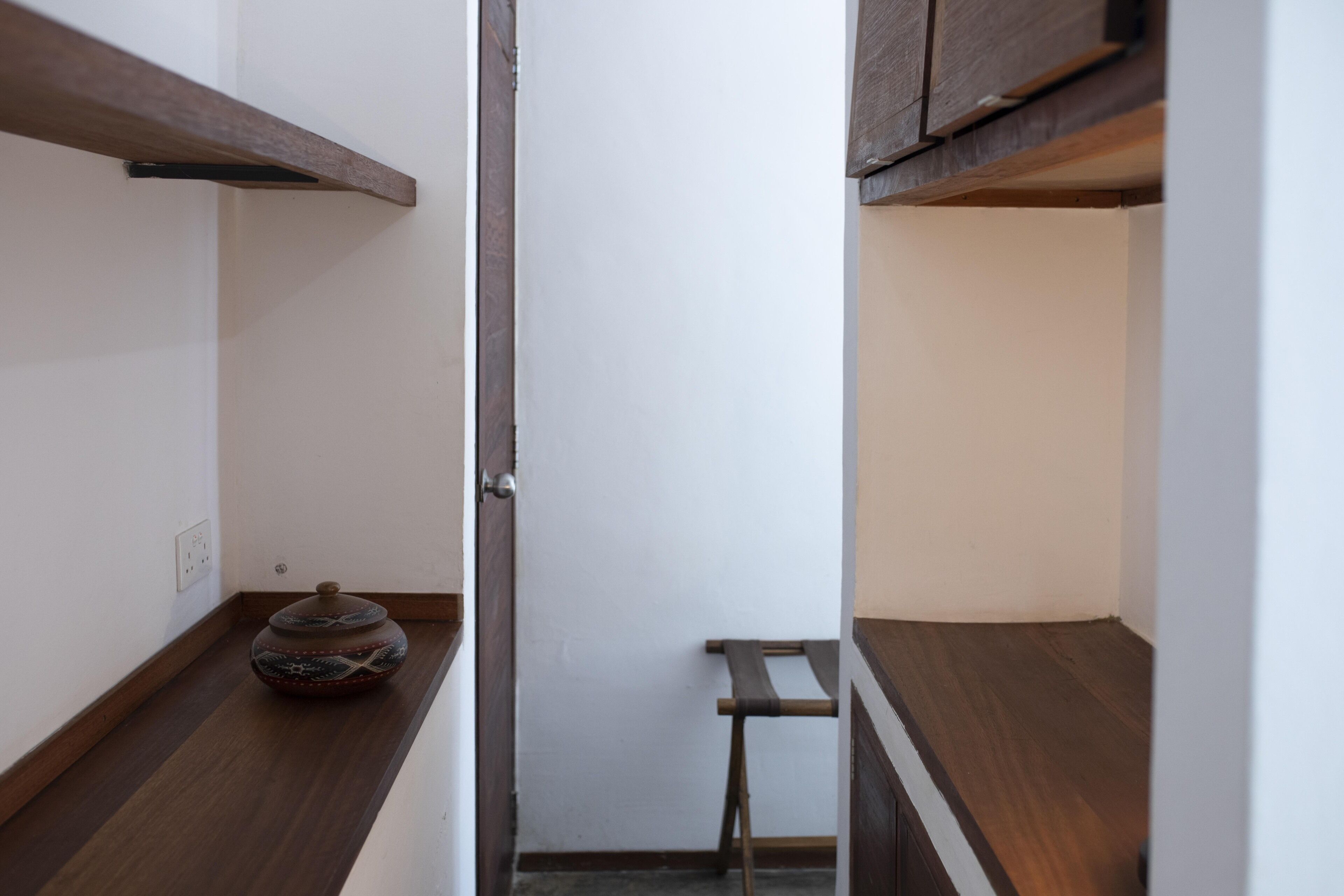 A narrow hallway with wooden flooring, a small table with a decorative pot, and a door with a metal handle.