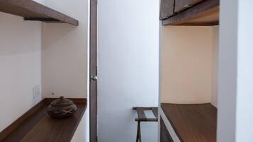 A narrow hallway with wooden flooring, a small table with a decorative pot, and a door with a metal handle.