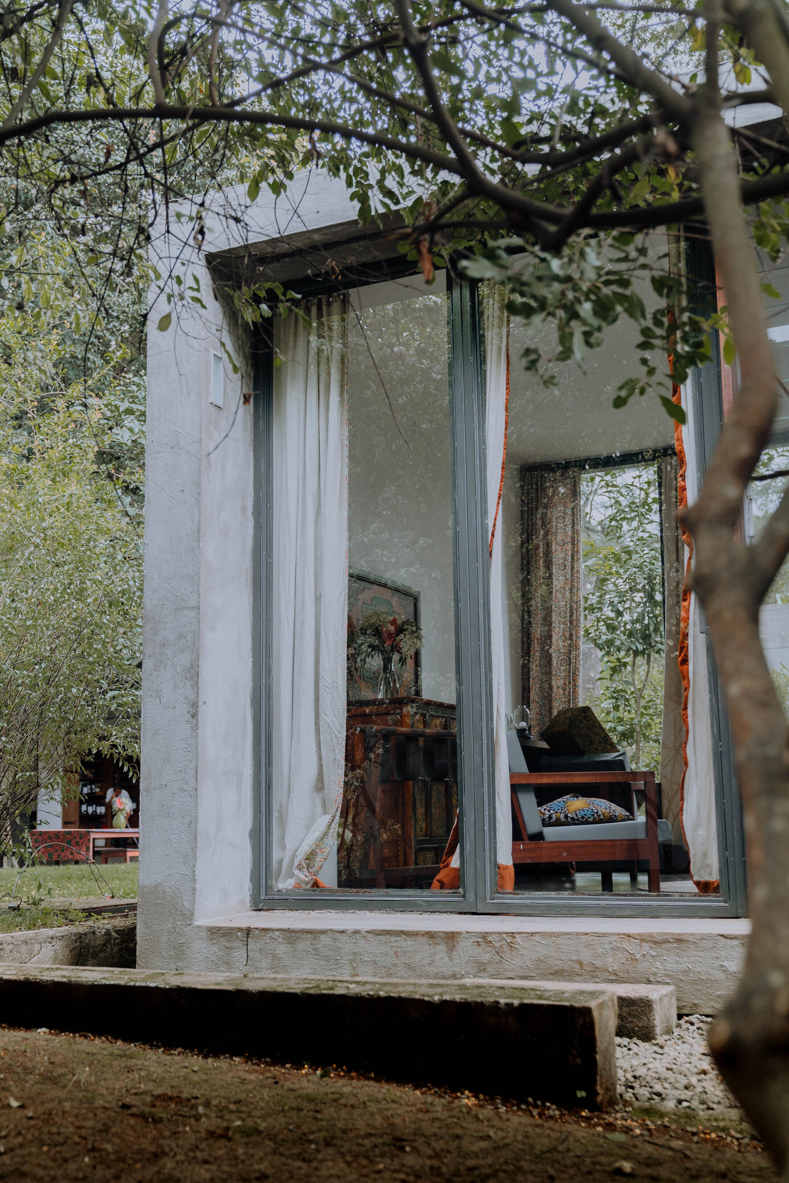A small, enclosed outdoor seating area with a chair and a table, surrounded by a white wall and curtains.