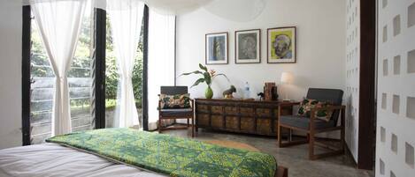 Une chambre à coucher avec un grand lit, un bureau, deux chaises, un vase et des œuvres d’art encadrées accrochées au mur.