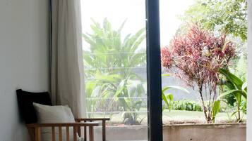 A bedroom with a large bed, a wooden chair, a window with a view of greenery and a tree.