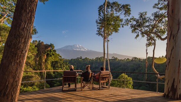 A wooden deck with two wooden chairs facing a scenic view of a mountain. - Kaliwa Lodge (Machame)