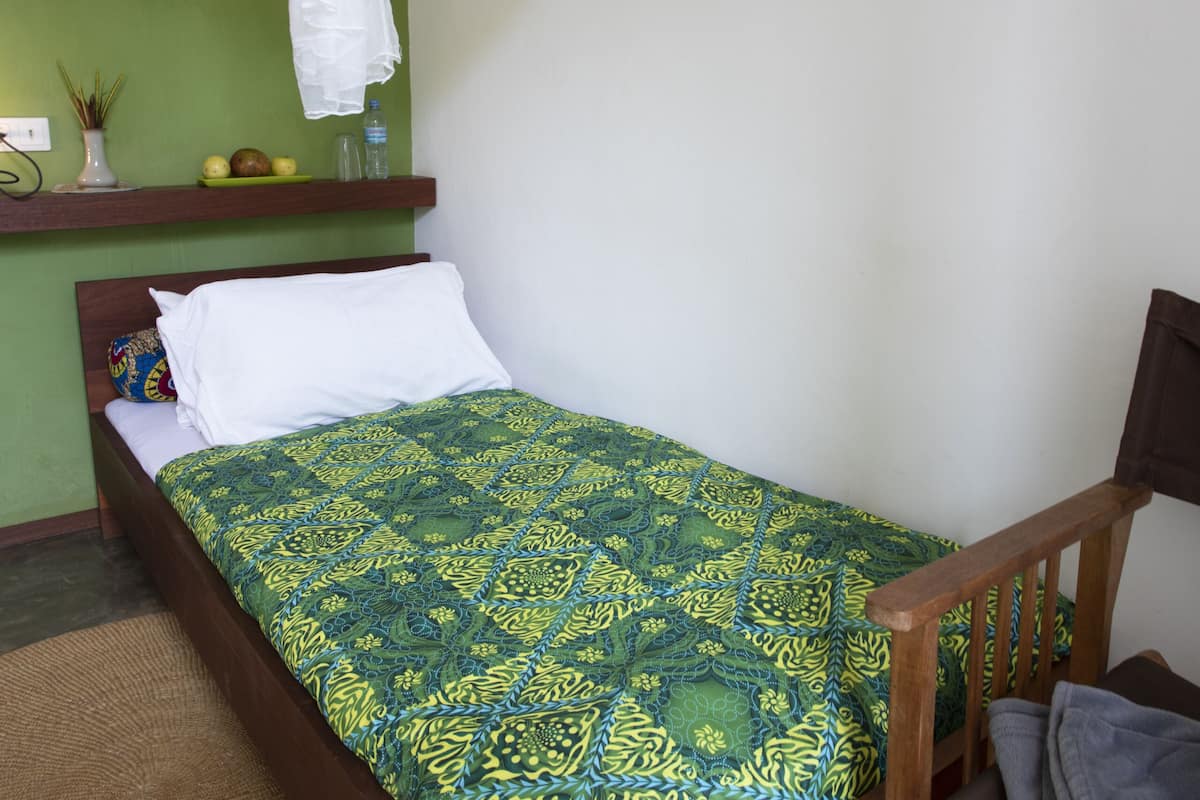 A bedroom with a bed, a chair, a hanging mosquito net, a wall art of zebras, and a shelf with a vase and fruits.