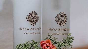 Dos botellas de Inaya Zanzibar African Essentials sobre una superficie blanca, adornadas con flores decorativas.