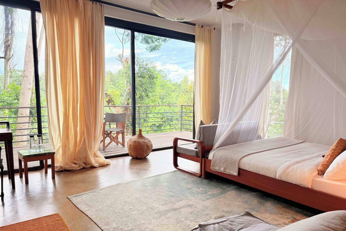 A bedroom with a large window, a bed, a chair, and a table.
