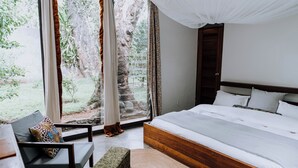 A bedroom with a large bed, a bench, and a view of the outdoors. - Kaliwa Lodge (Machame)