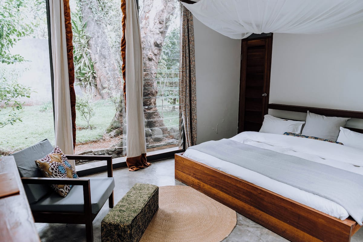 A bedroom with a large bed, a bench, and a view of the outdoors.