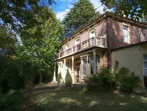 A two-story brick house with a balcony, surrounded by lush greenery. - Lucinda B&B (Latrobe)
