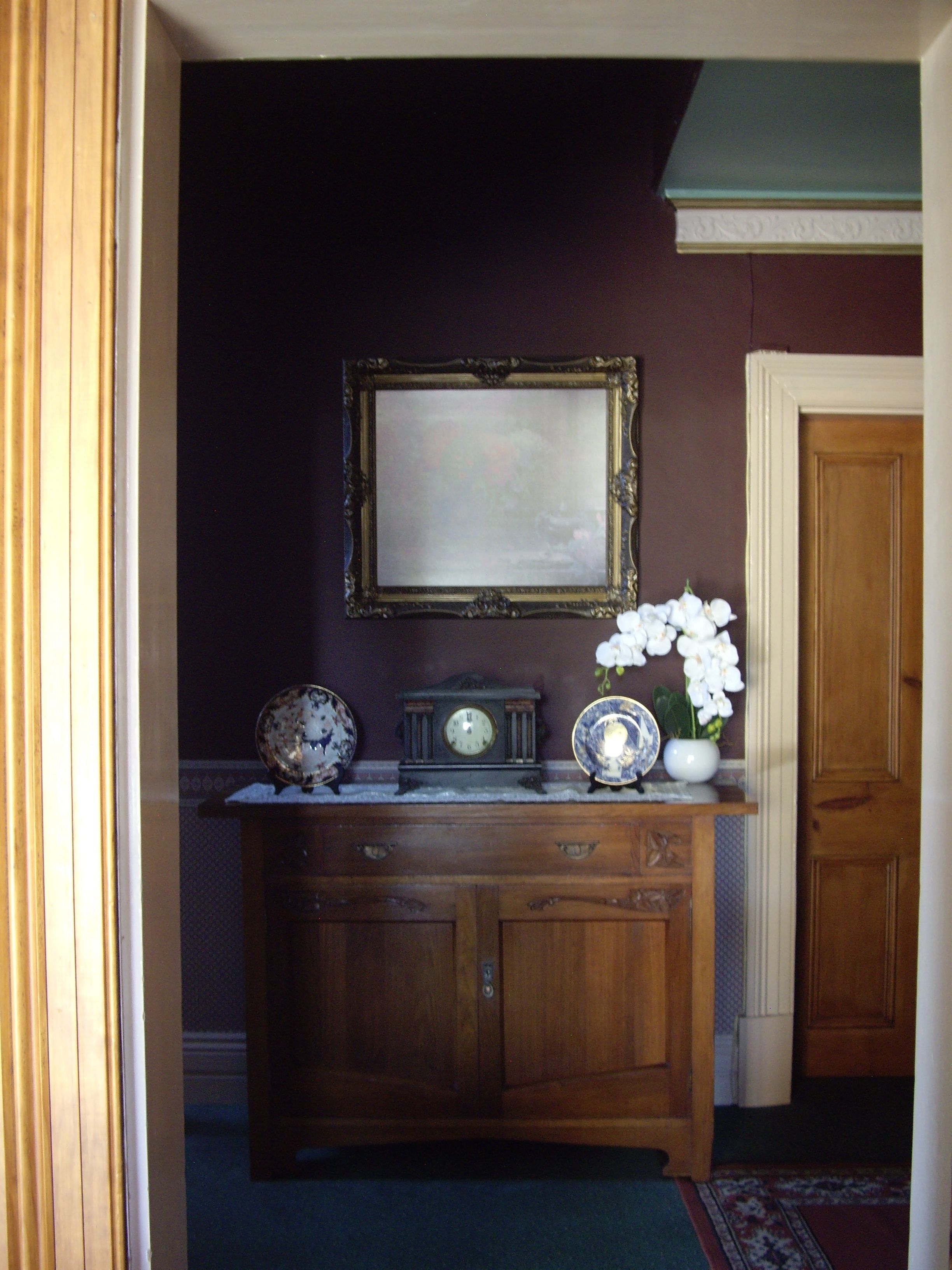 A wooden console table with a clock and decorative plates, a framed mirror on the wall, and a door to the right.