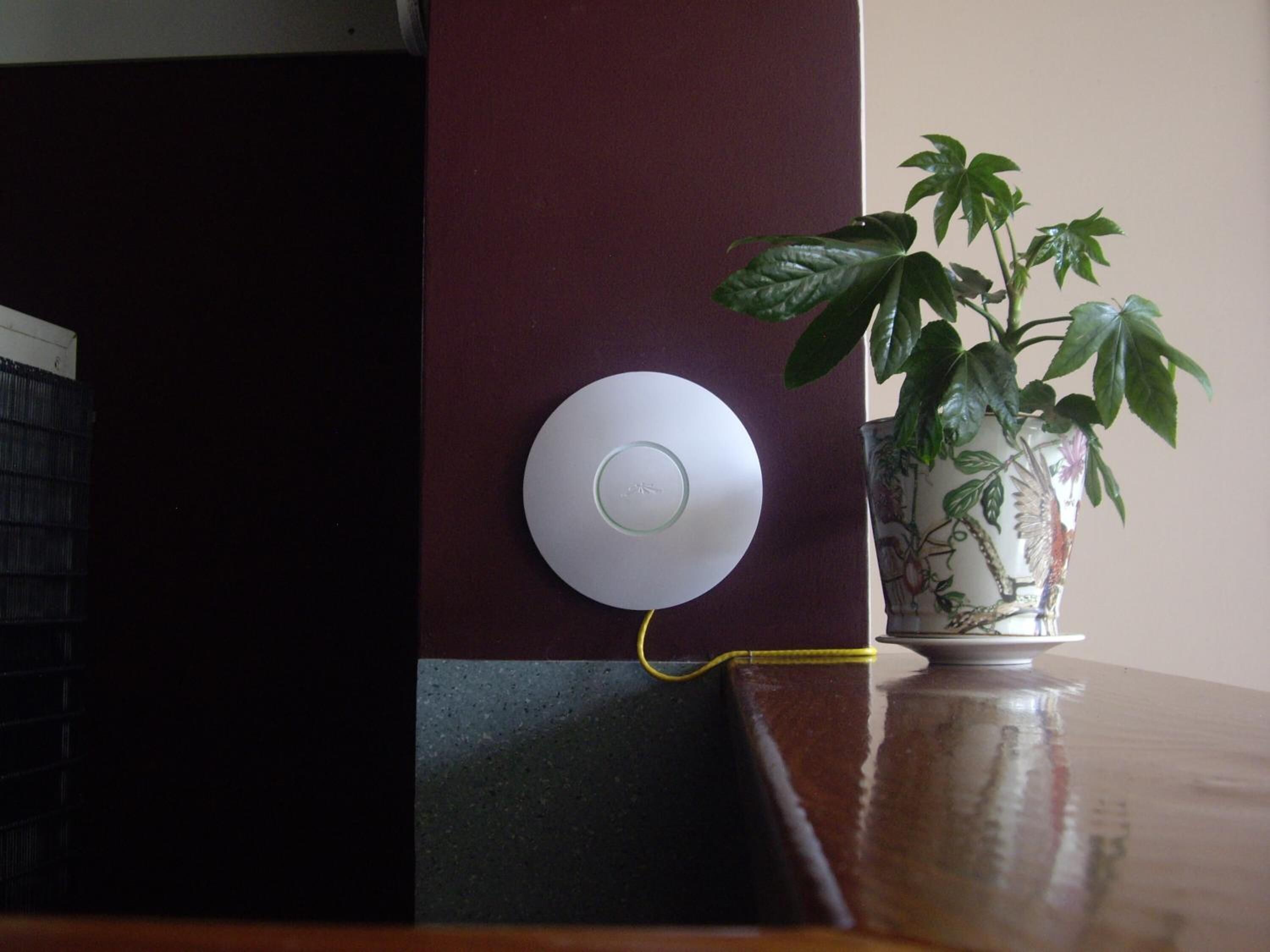 A white circular device mounted on a dark wall, connected by a yellow cable.