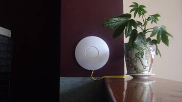 A white circular device mounted on a dark wall, connected by a yellow cable.