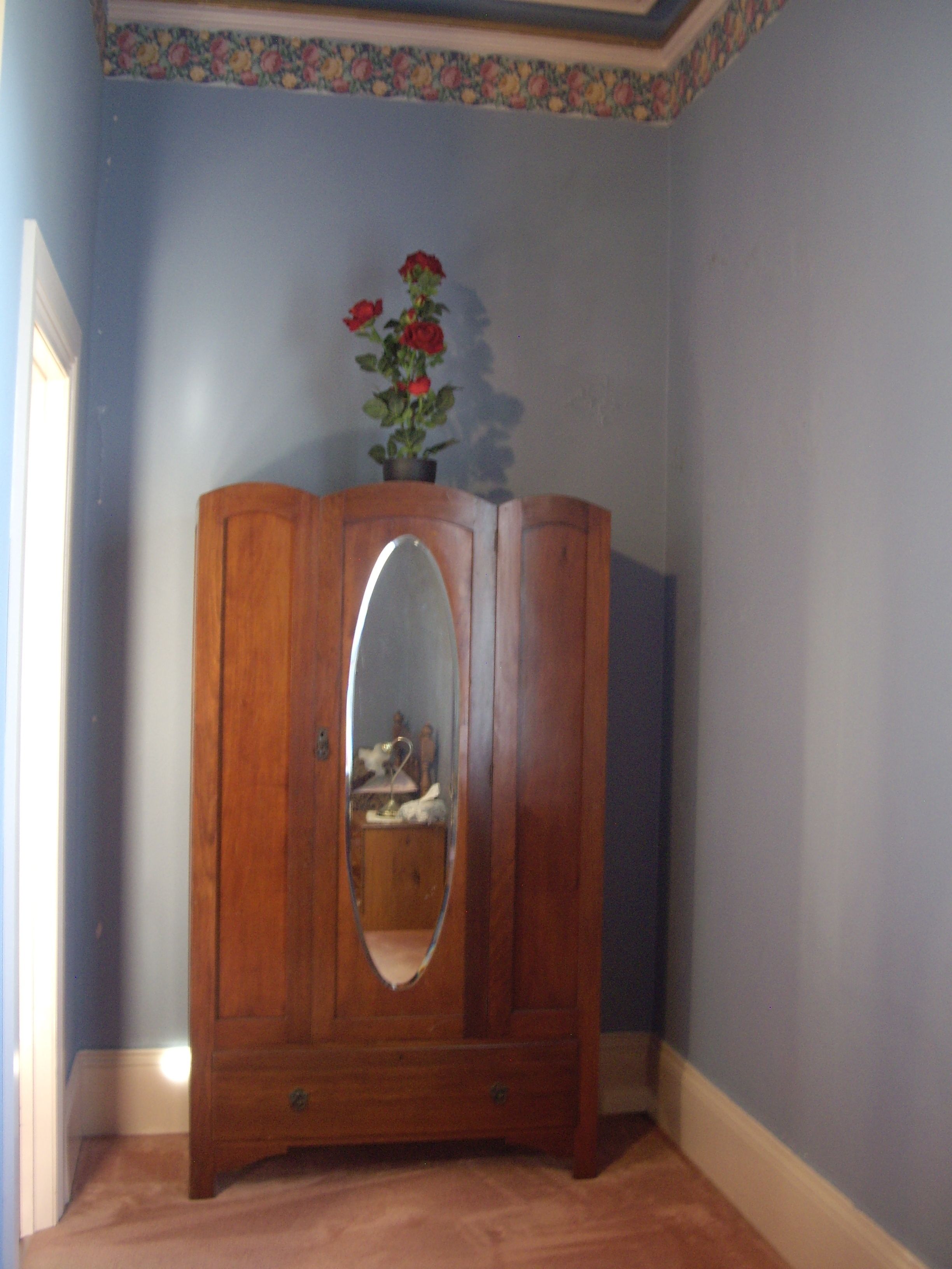 Une armoire en bois avec un miroir, une plante en pot aux fleurs rouges et un motif floral sur le mur.