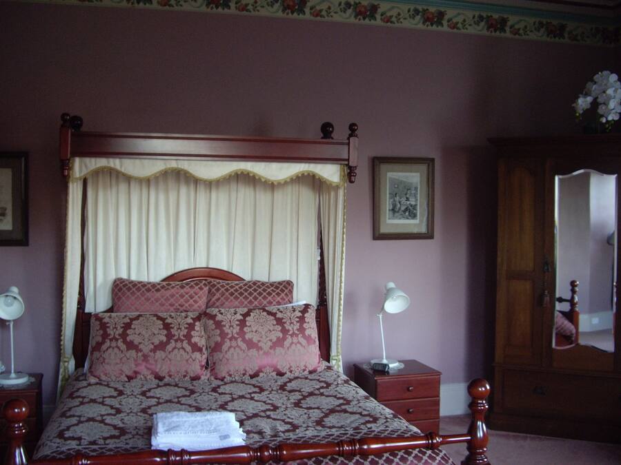 A bedroom with a four-poster bed, a nightstand with a lamp, a dresser, and a mirror.