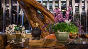 Un mostrador de recepción con una escultura de madera, una mesa de cristal y varias plantas en macetas.