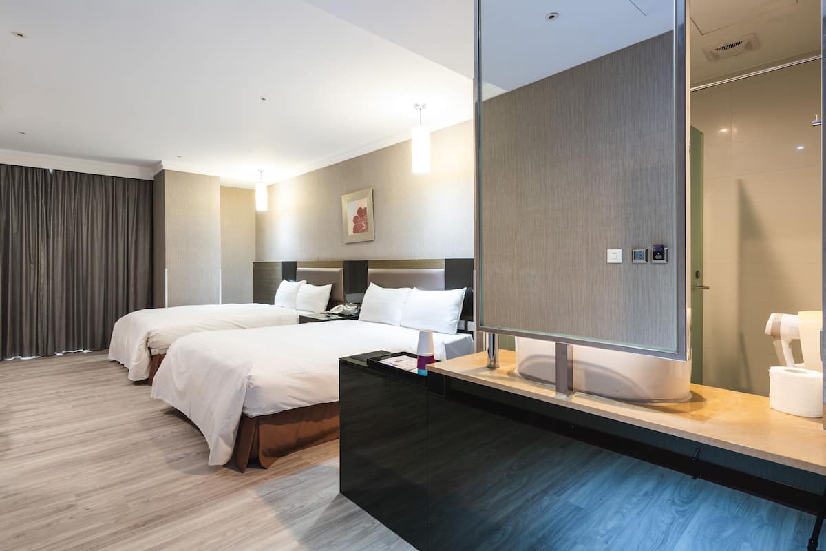 Habitación de hotel moderna con dos camas, un espejo grande, tocador con lavamanos y zona de ducha.