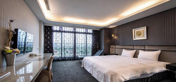 A modern hotel room with a large bed, a desk with a chair, a bedside table, a lamp, and a window with a view. - Shianghu Boutique Hotel (Chiayi City)