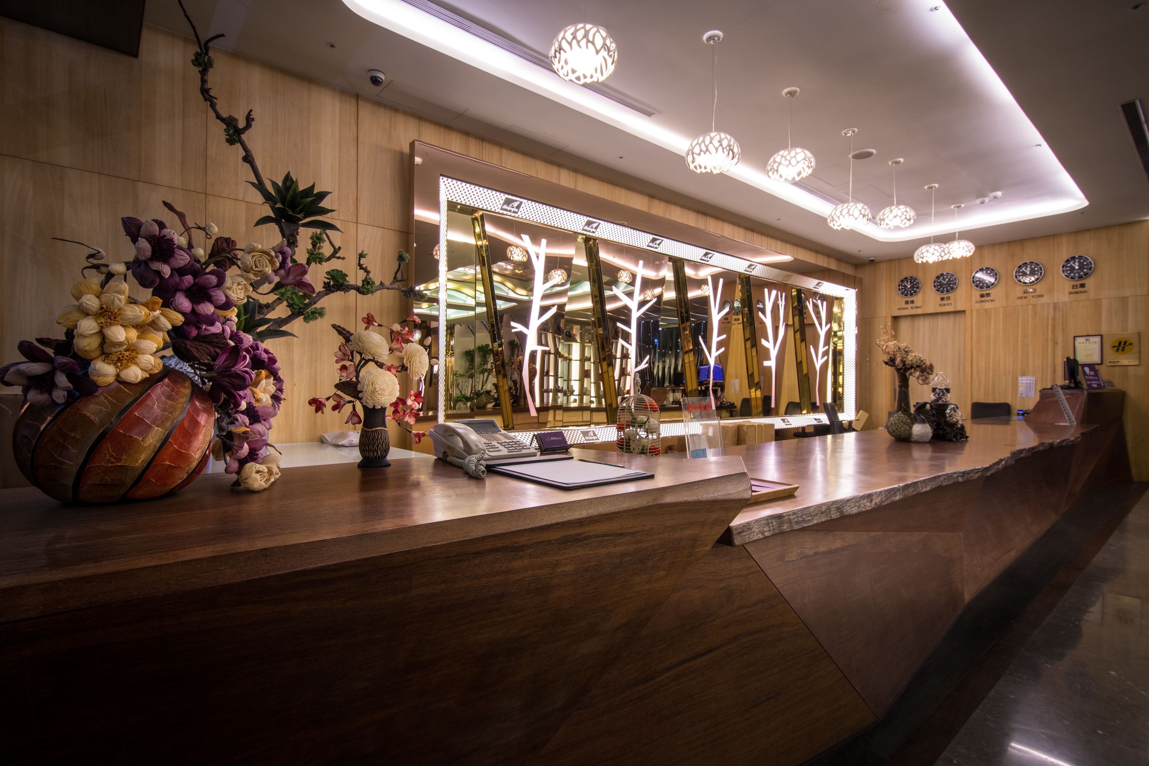 A reception desk with a modern design, featuring a wooden counter, a telephone, a notepad, and a vase with flowers.