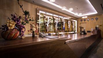 A reception desk with a modern design, featuring a wooden counter, a telephone, a notepad, and a vase with flowers.