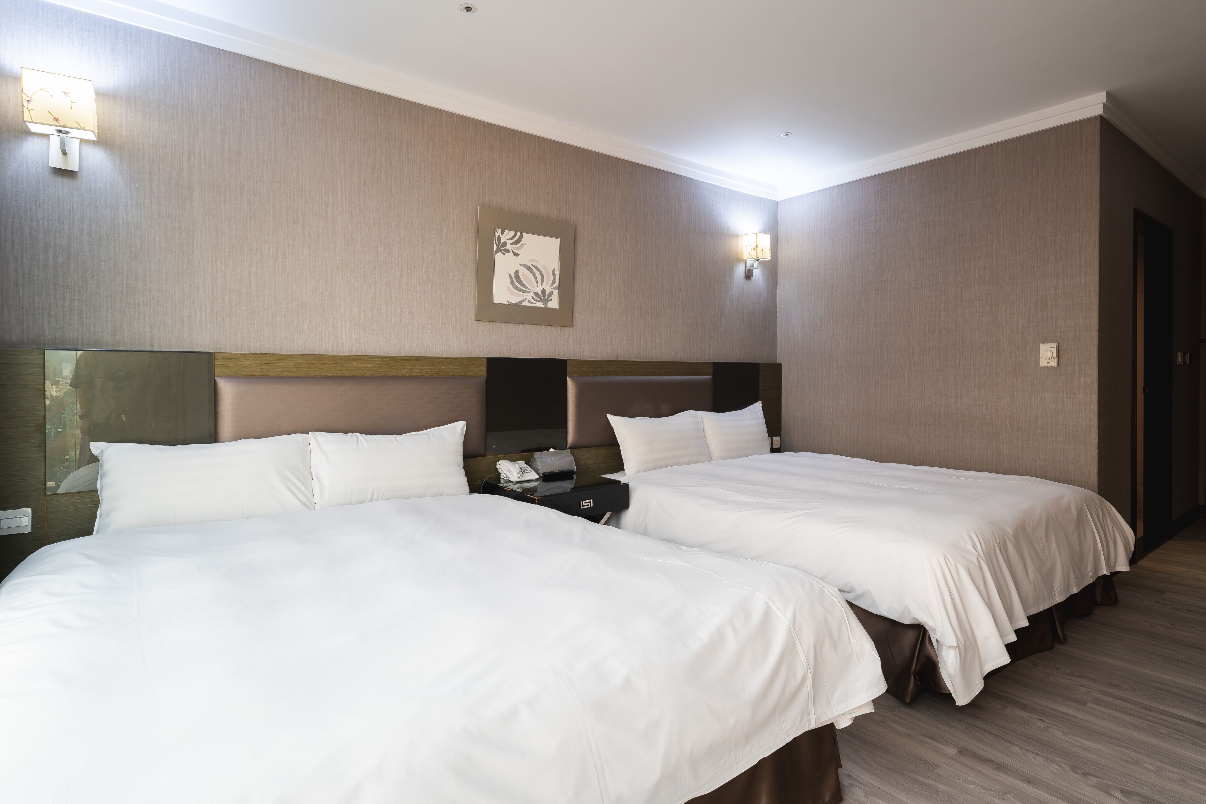 Una habitación de hotel con dos camas, una mesita de noche, una lámpara y un cuadro en la pared.