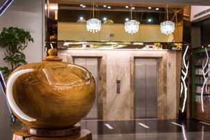 Un tazón de madera grande sobre un pedestal de madera en un vestíbulo moderno con una pared de mármol y un mostrador de vidrio al fondo.