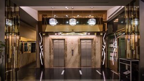 Un área de ascensor moderna con paredes de mármol, puerta de ascensor de vidrio y un atril para revistas.