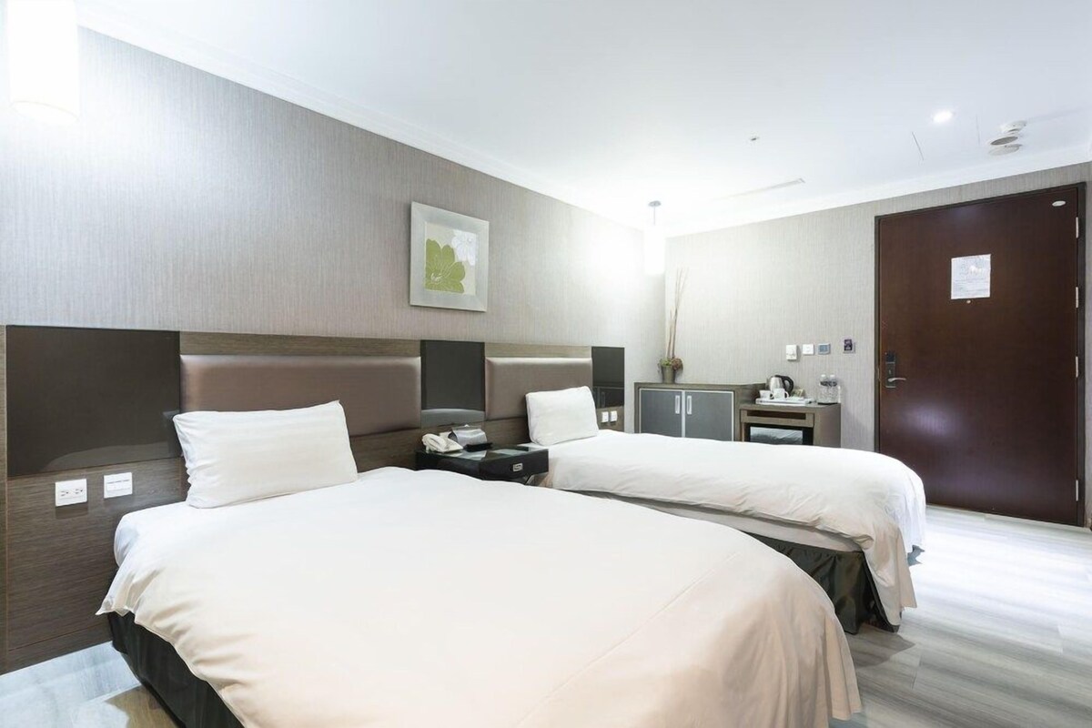 Ein Hotelzimmer mit zwei Betten, einem Schreibtisch, einem Stuhl, einem Kleiderschrank und einer Tür.