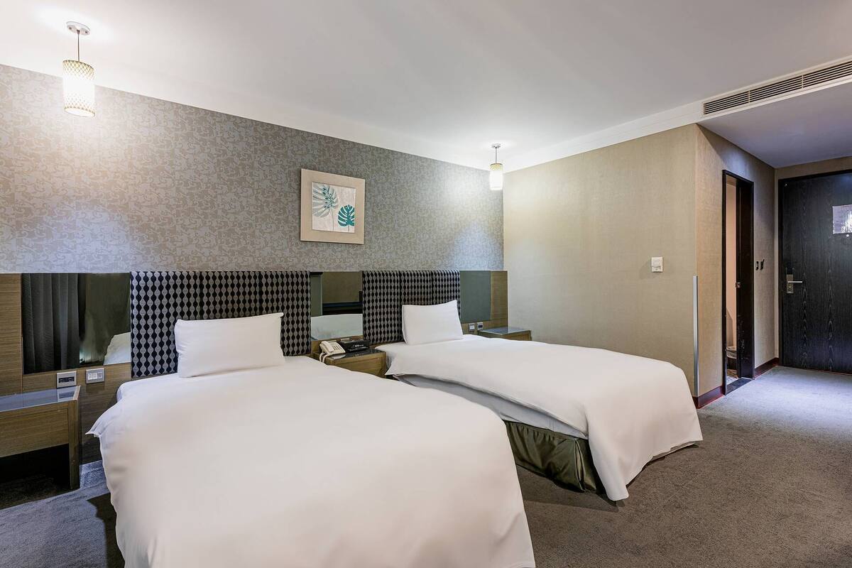 Habitación de hotel con dos camas, un espejo grande, una obra de arte enmarcada y una puerta que da a otra habitación.