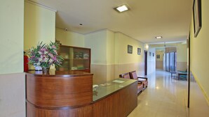 Una recepción con encimera de madera y cristal, una planta en maceta y un banco al fondo.
