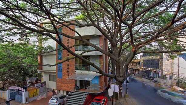 Un edificio de varios pisos con una escalera que conduce a la entrada, coches aparcados y un árbol en primer plano.