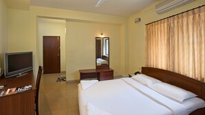 Una habitación de hotel con cama, escritorio con televisor, espejo y ventilador de techo.