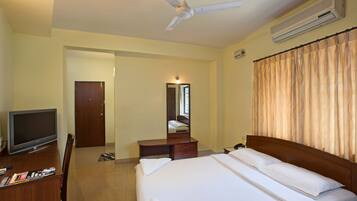 A hotel room with a bed, a desk with a TV, a mirror, and a ceiling fan.