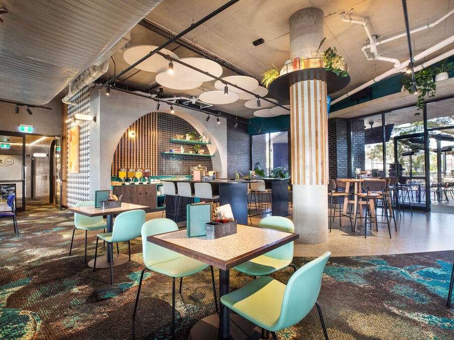 Un café moderno con una zona de bar, asientos sobre una alfombra estampada y una señal de salida visible.