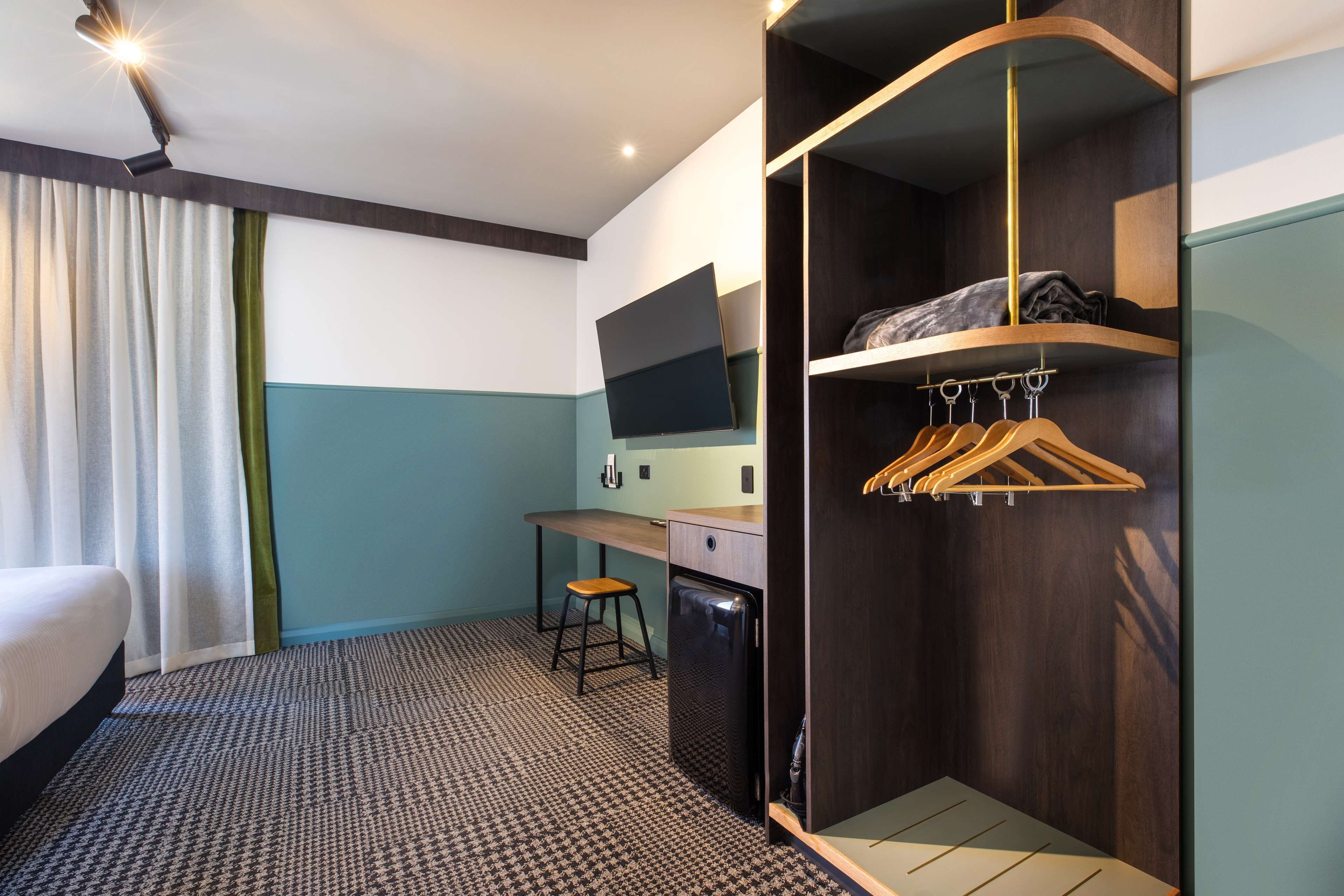 Ein Hotelzimmer mit einem Bett, einem Schreibtisch, einem Stuhl, einem Kleiderschrank und einem Fernseher.