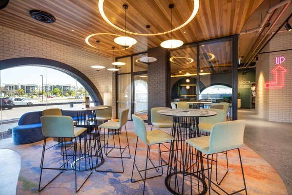 A modern cafe with round tables and chairs, large windows, and a brick wall. - Nightelier Mitchelton The Brook (Mitchelton)