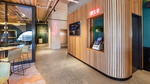 Un área de recepción moderna con un mostrador de madera, un quiosco digital y una pared de cristal con vistas al interior.