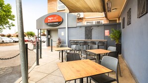 Un área de estar al aire libre con mesas y sillas, un letrero que dice 'Nightcap Bistro & Gaming', y un muro de ladrillo al fondo.