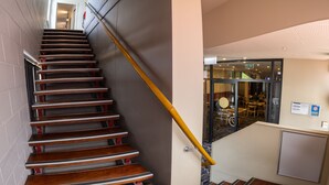 Una escalera con escalones de madera y baranda metálica, que lleva a una habitación con puerta de vidrio y un letrero que dice "bistro gaming".