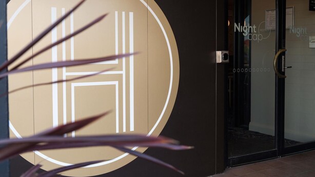 Entrada de un hotel con un logotipo circular, puerta de cristal y un letrero con el número 8.