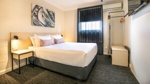 Habitación de hotel moderna con una cama grande, una mesita de noche, una obra de arte colgada en la pared, una zona de ducha y un pequeño rincón de estar.