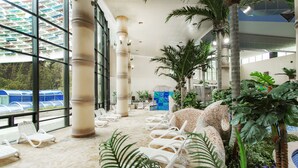 A spacious indoor area with white lounge chairs, large windows, and tropical plants. - Lotte Buyeo Resort (Buyeo)