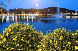 A serene lakeside view with a traditional pavilion, a fountain, and a well-maintained flower bed.