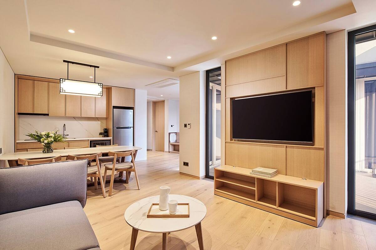 A modern living room with a flat-screen TV, wooden cabinetry, a dining area, and a sofa.