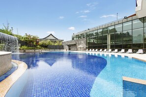 A swimming pool with a tiled edge, a waterfall feature, and a modern building with large windows in the background.