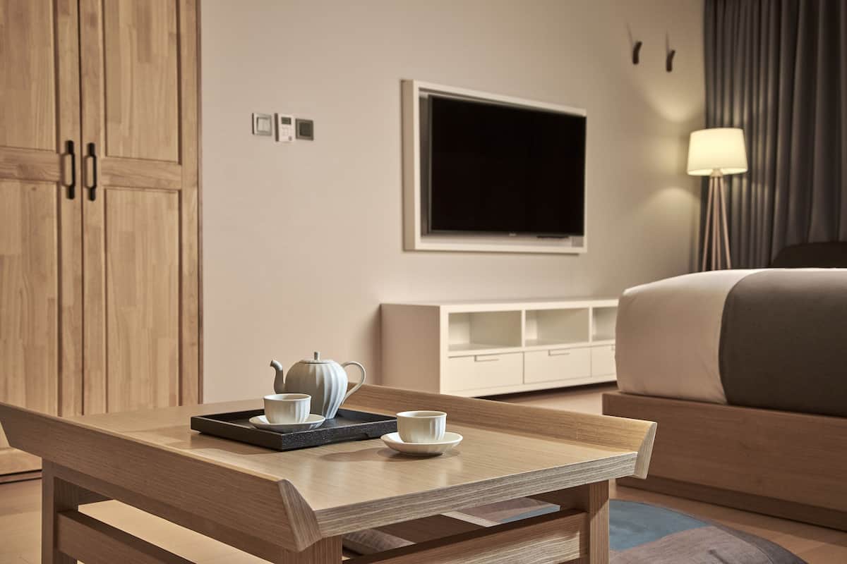 A modern hotel room with a wooden desk, a flat-screen TV, a bed, and a bedside lamp.