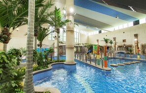An indoor swimming pool with multiple lanes, palm trees, and a water slide. - Lotte Buyeo Resort (Buyeo)