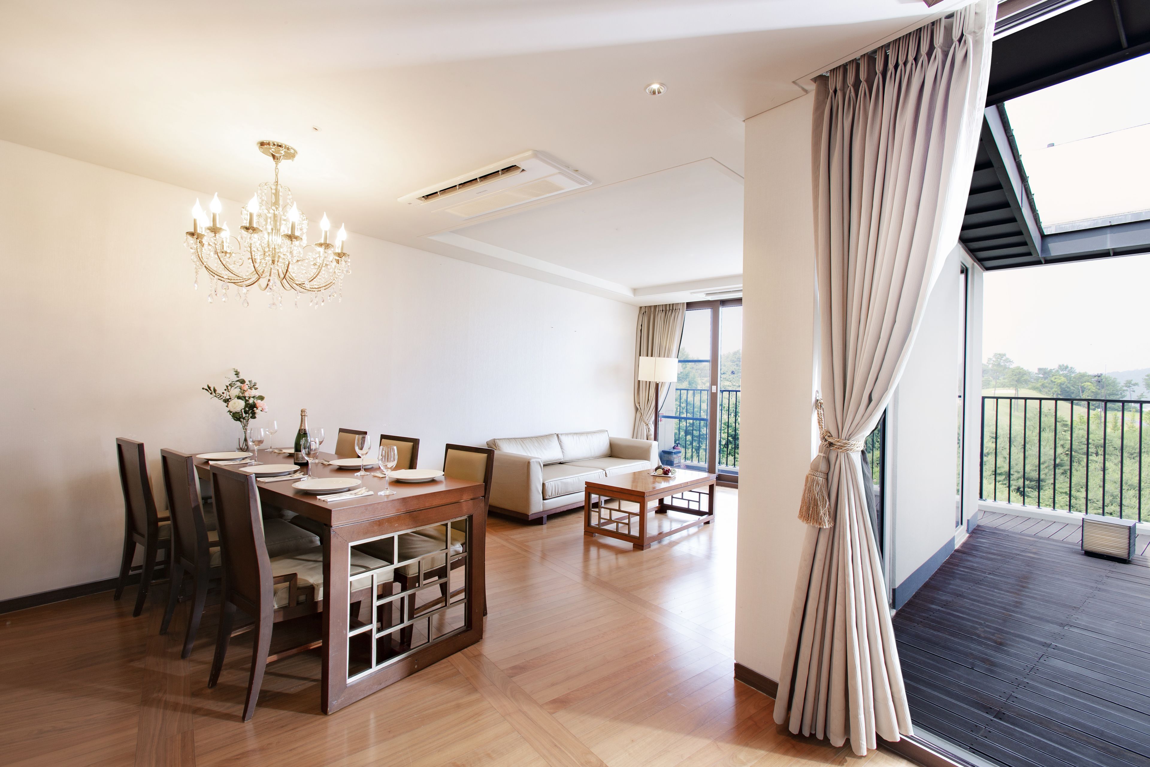 A spacious living area with a dining table, sofa, and a balcony with a view.