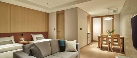 Una habitación de hotel moderna con sofá, dos camas, una mesa de comedor con sillas y televisión.